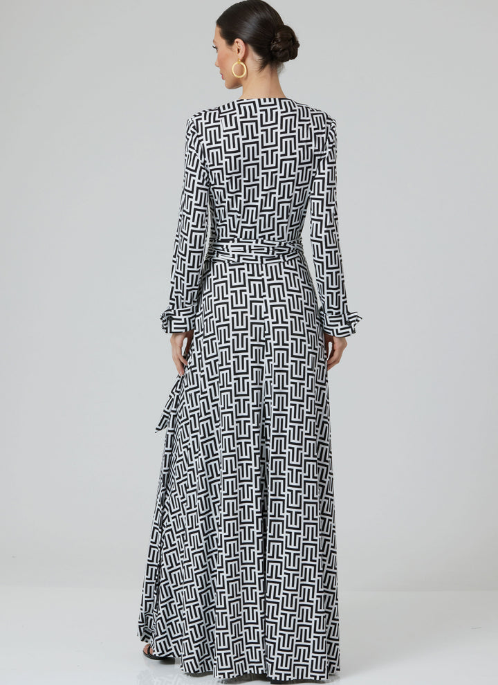 A woman with a low bun and hoop earrings models the Super Cheap Fabrics Pattern - Vogue - V2000 - Misses’ DVF Wrap Dress by Diane von Furstenberg, featuring long sleeves and a black and white geometric print, against a plain light gray background.