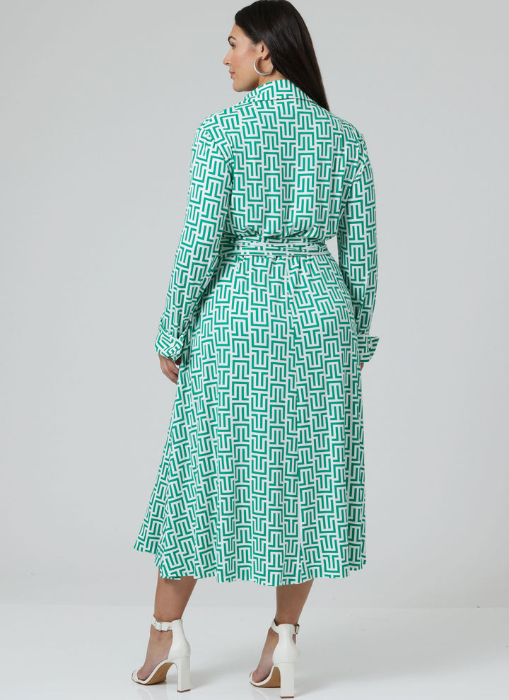 A woman with long dark hair wears the Super Cheap Fabrics Pattern - Vogue V2000 Misses’ DVF Wrap Dress by Diane von Furstenberg, featuring a green and white print, belted waist, and white heeled sandals against a light gray background.