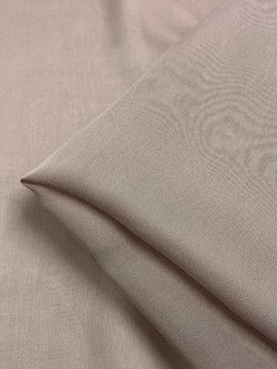 A close-up image of a piece of Silk Georgette - Quail from Super Cheap Fabrics, folded neatly. The light beige fabric exhibits a smooth and slightly reflective texture, indicating its fine, lightweight nature. The sharply defined edges of the fold suggest careful handling, making it ideal for crafting elegant summer outfits.