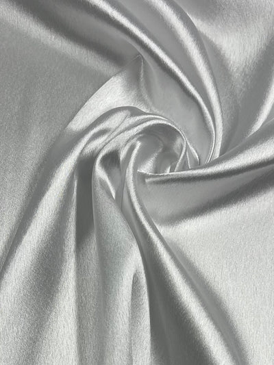 A close-up of the Satin Back Crepe - White - 150cm from Super Cheap Fabrics, draped and gathered in soft folds, creating a swirling pattern in the center. This versatile fabric showcases a smooth, shiny surface with a lustrous sheen, reflecting light and highlighting its silky texture.