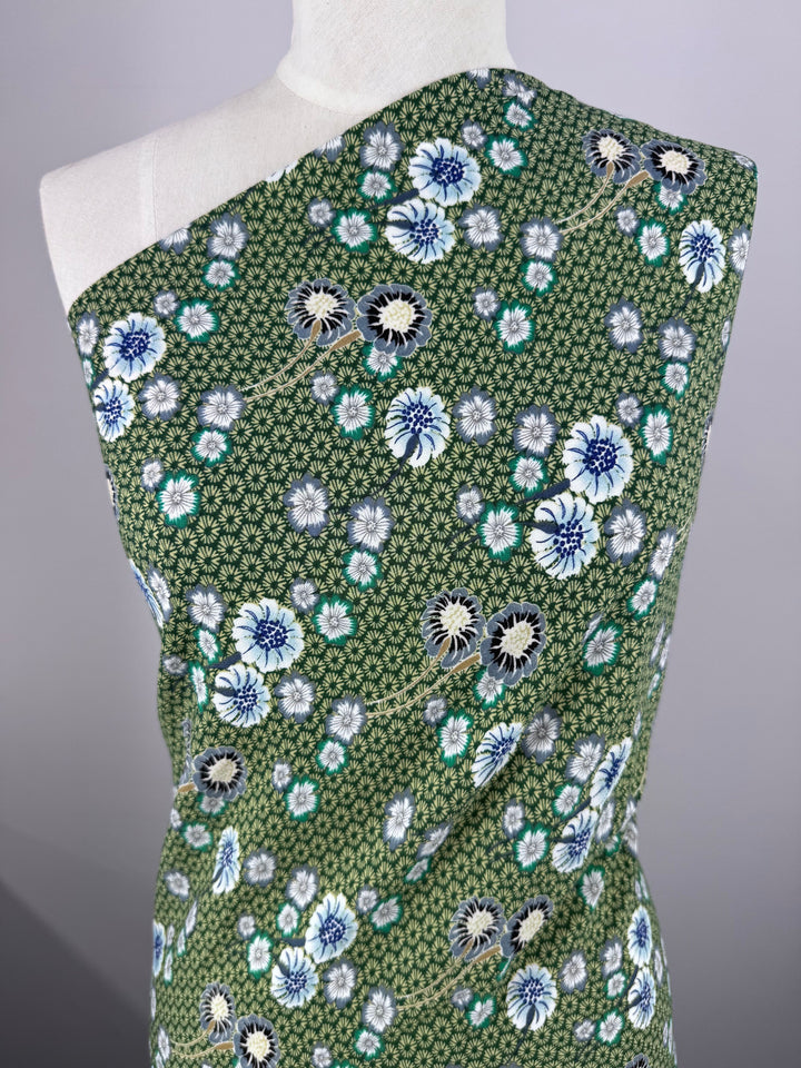 Displayed on the mannequin is a green "Printed Crepe - Botan - 148cm" from Super Cheap Fabrics, showcasing a pattern of white, blue, and black flowers with small geometric shapes arranged diagonally.
