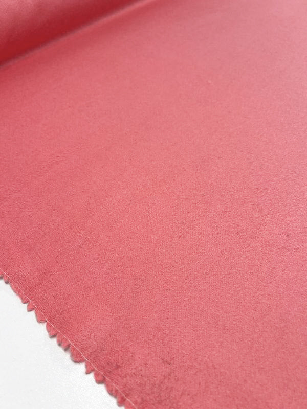 A close-up image of the "Wool Cashmere - Shell Pink - 150cm" fabric by Super Cheap Fabrics, featuring evenly spaced, small cutouts along the edge. The texture appears soft with a slightly matte finish, showcasing its luxurious feel and heavy weight. It is spread out flat on a smooth white surface.