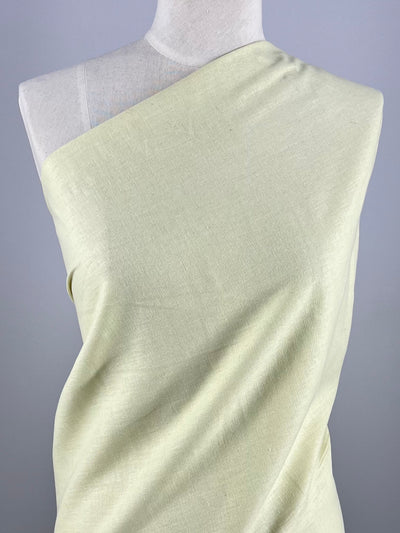 A mannequin is draped in Super Cheap Fabrics’ Plain Linen - Dusty Yellow (140cm), styled diagonally from one shoulder to the opposite underarm, set against a plain light gray background.