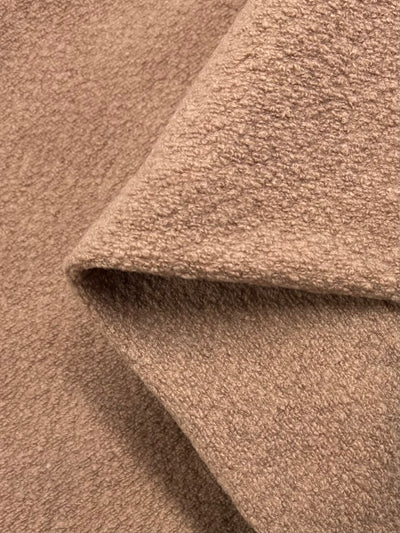 Close-up image of a textured, light brown fabric with a visible fold. The texture resembles soft fleece or wool, showcasing a slightly rough yet cozy surface. This Boiled Wool - Tuscany - 135cm from Super Cheap Fabrics appears warm and suitable for cold weather apparel or home textiles.